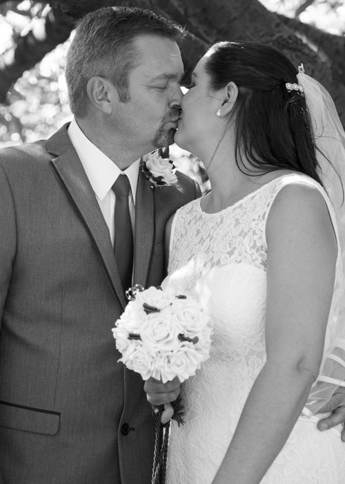 black and white couples photograph on their wedding day kissing underneath a tree at the stables