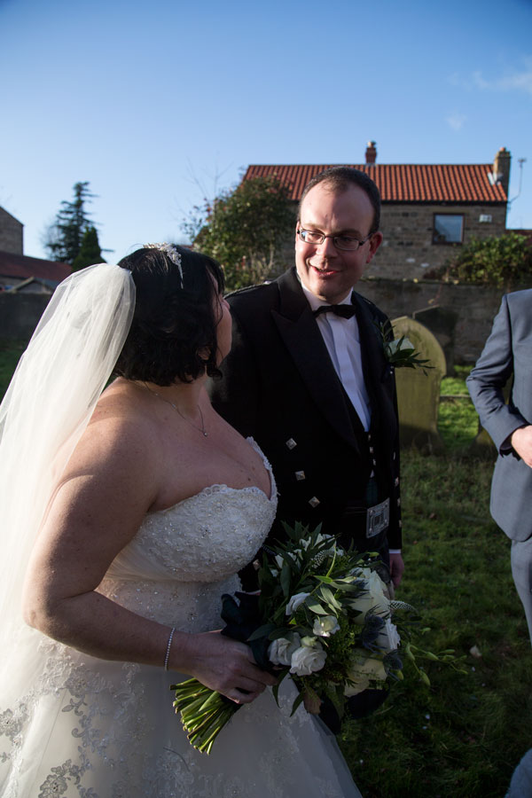 Groom smiling at bride in the grounds of St John the Baptist church Adwick upon Dearne