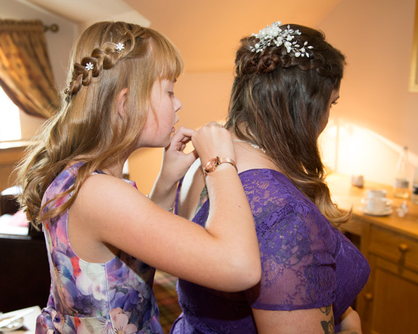 Bridesmaids fastening each others purple bridesmaid dresses in the three acres inn bridal suite