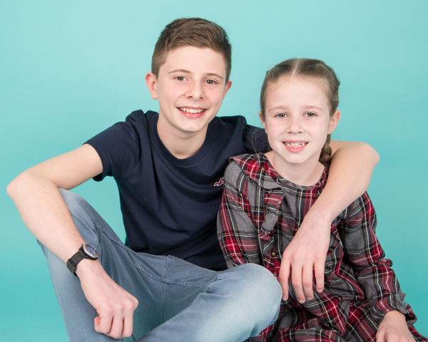 Brother and sister sitting together against a blue backdrop family photo shoot barnsley