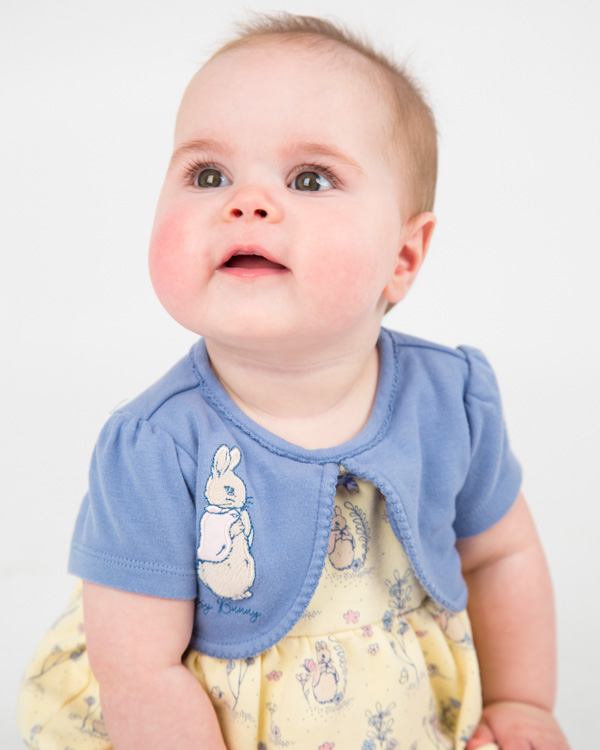 Baby girl in peter rabbit dress looking up with large eyes